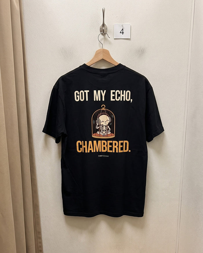 The Got My Echo Chambered tee on a wooden hanger against a plain wall, back print facing out: a skeleton in a birdcage wearing headphones.